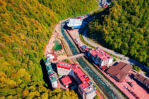 Фото: Горный курорт Сочи с высоты птичьего полета – отели и набережная вдоль реки в окружении осеннего леса, прекрасное место для отдыха.